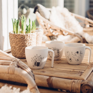 Muumimukeja rottinkipöydällä parvekkeella auringonpaisteessa.